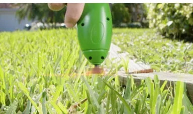 Cordless handheld lawn trimmer with extension pole and protective shield on a garden lawn.