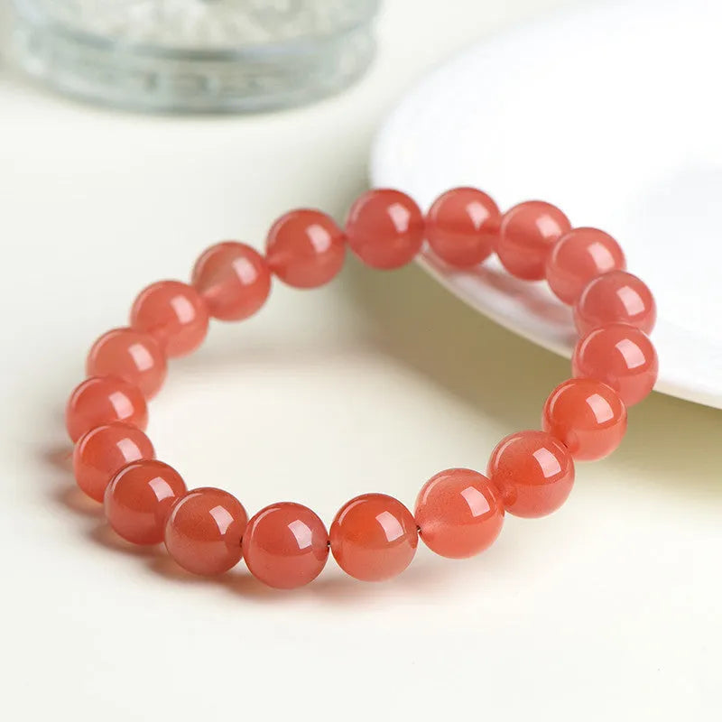Loose polished cherry red agate beads in various sizes for bracelet making on a white surface.