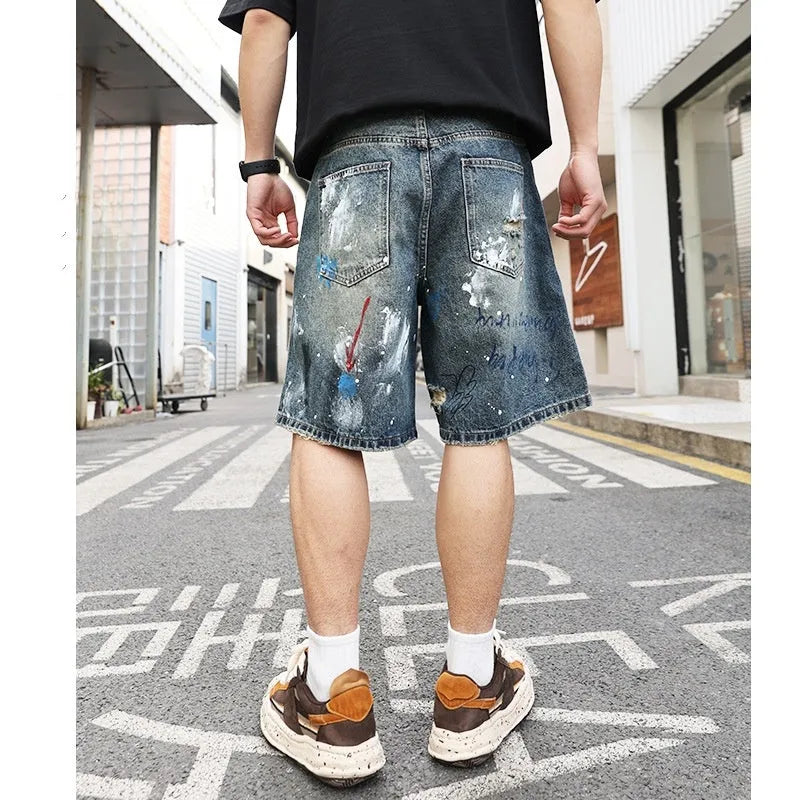 Blue men's denim shorts with ripped knees and graffiti-style print, featuring a straight leg and zipper fly.