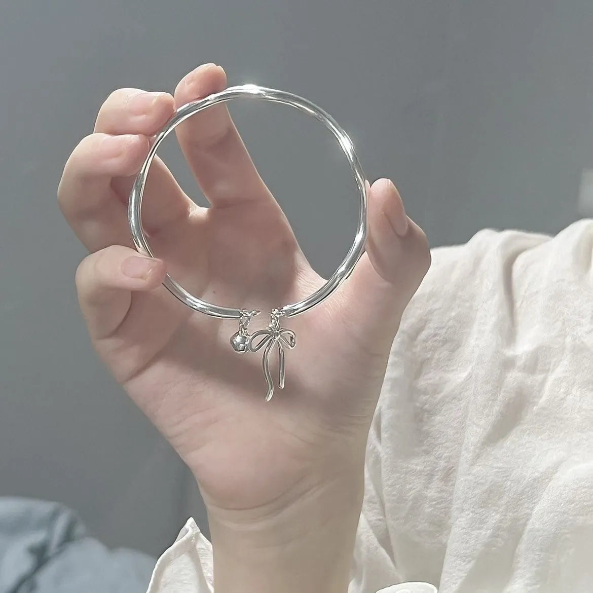 Silver adjustable bracelet with bow-shaped clasp on wrist, showing zinc alloy electroplated construction
