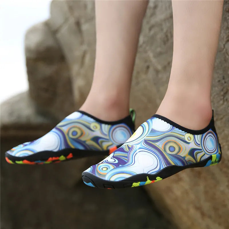 Pair of blue Lycra beach wading shoes with EVA midsole on a sandy beach background.