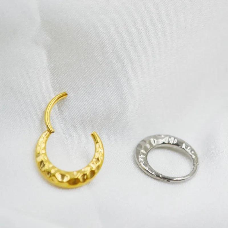 Close-up of a concave-convex titanium nose ring in gold or silver finish, showing textured surface.