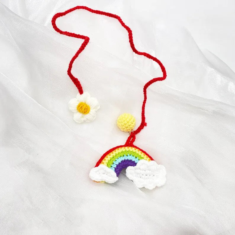 Handmade crocheted avocado-shaped car pendant with rainbow pattern, hanging.