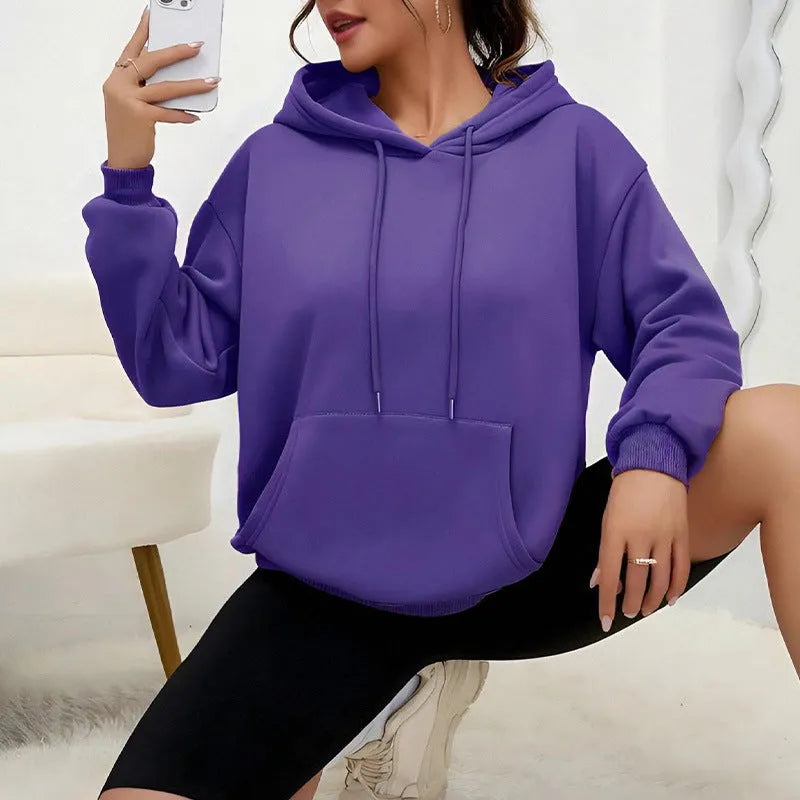 A woman wearing a loose grey drawstring hooded sweatshirt with a front pocket, showing the relaxed fit.