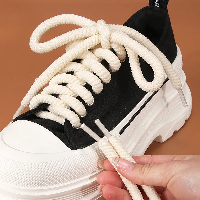 Round white woven shoelace with 10mm diameter next to a beige and black lace on a grey background.