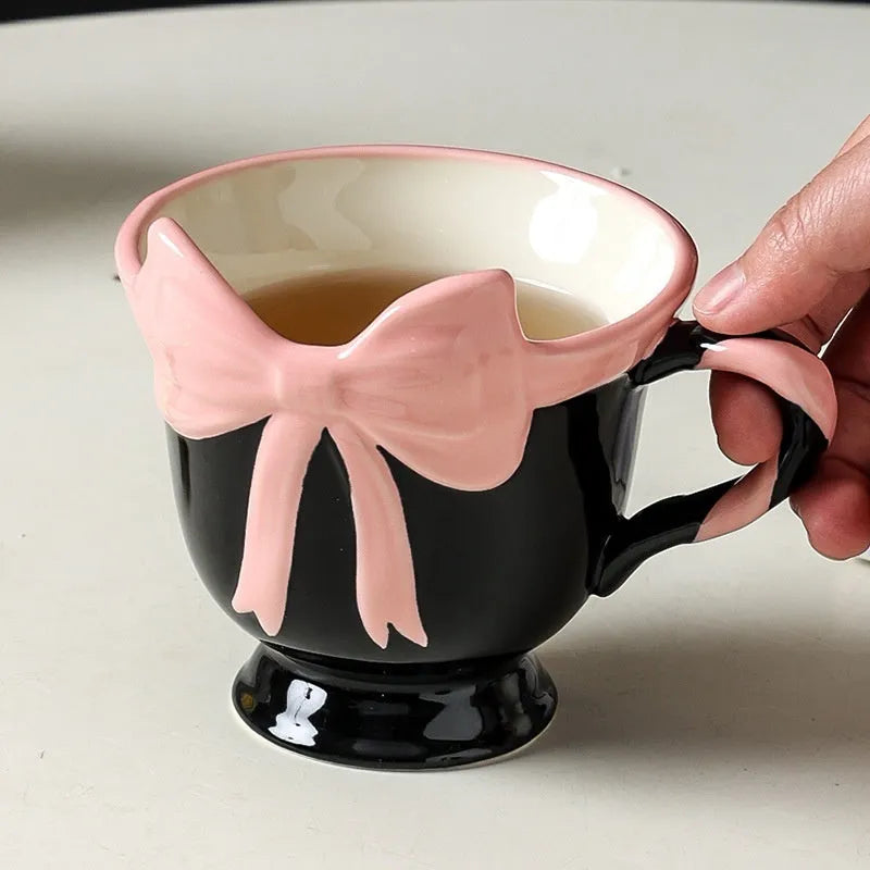 Cute white ceramic mug with a black heart bow design and printed handle ornament.