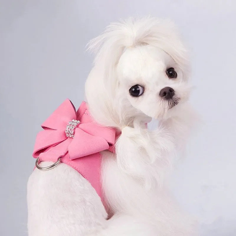 A pink microfiber puppy chest strap harness with a large central bowknot, showing adjustable buckles.