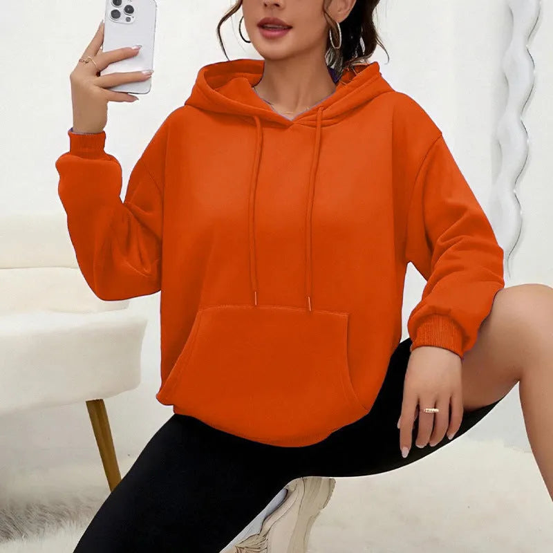 A woman wearing a loose grey drawstring hooded sweatshirt with a front pocket, showing the relaxed fit.