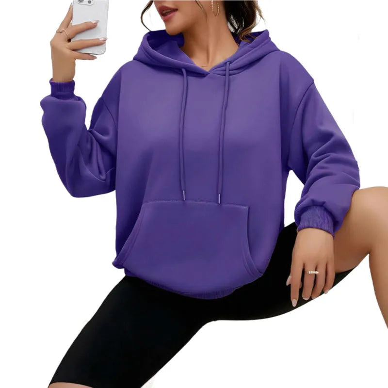 A woman wearing a loose grey drawstring hooded sweatshirt with a front pocket, showing the relaxed fit.