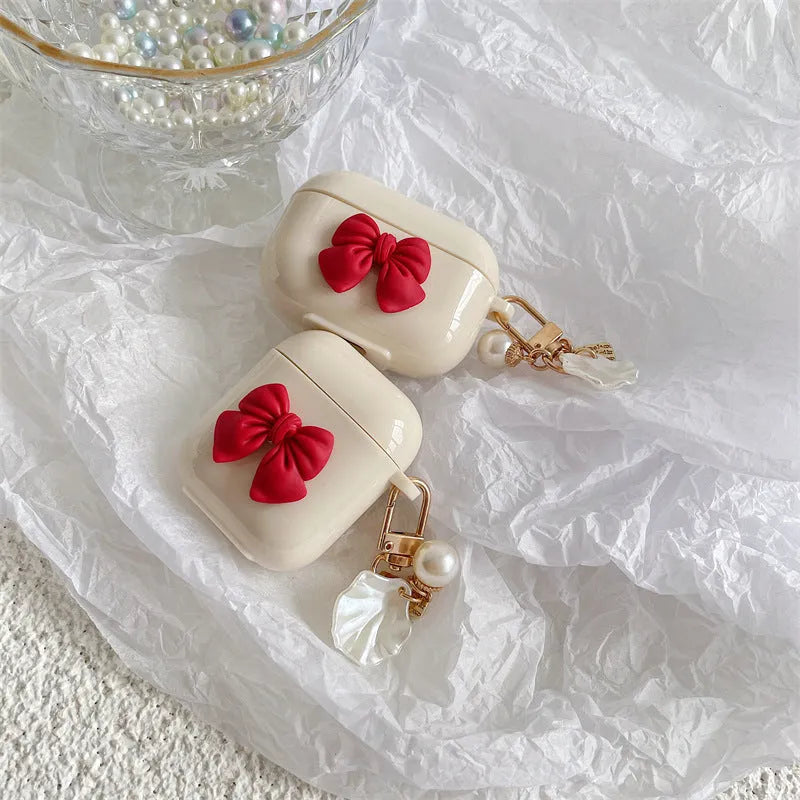 Beige and red TPU clamshell case with a bow pendant for AirPods 1, 2, 3 and Pro 3 models.