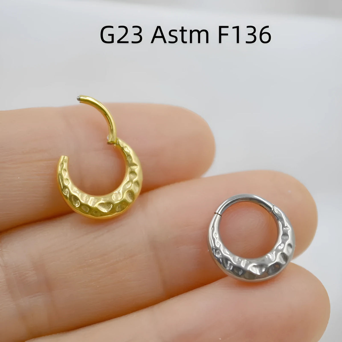 Close-up of a concave-convex titanium nose ring in gold or silver finish, showing textured surface.