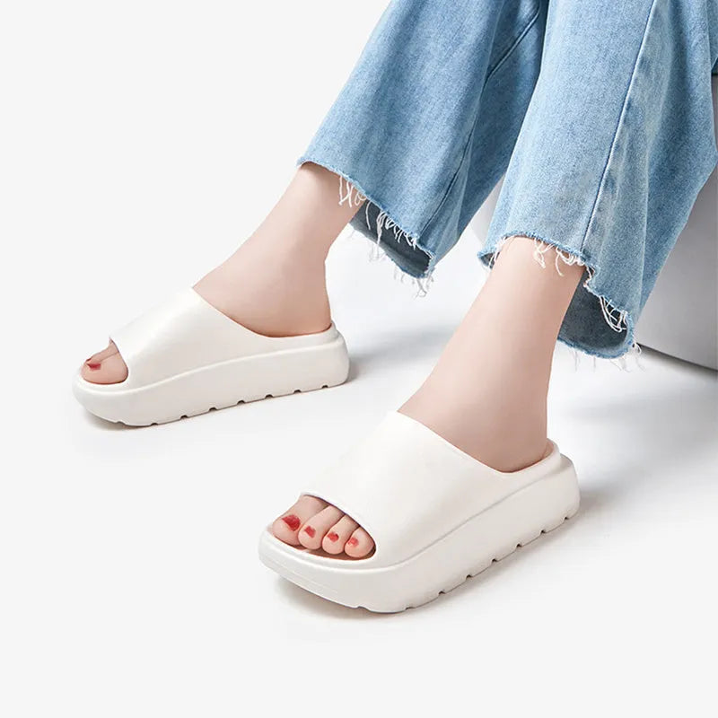 Women's thick-soled beige beach slippers with fish mouth design on a wooden deck.