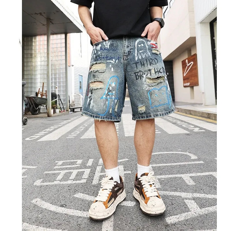 Blue men's denim shorts with ripped knees and graffiti-style print, featuring a straight leg and zipper fly.