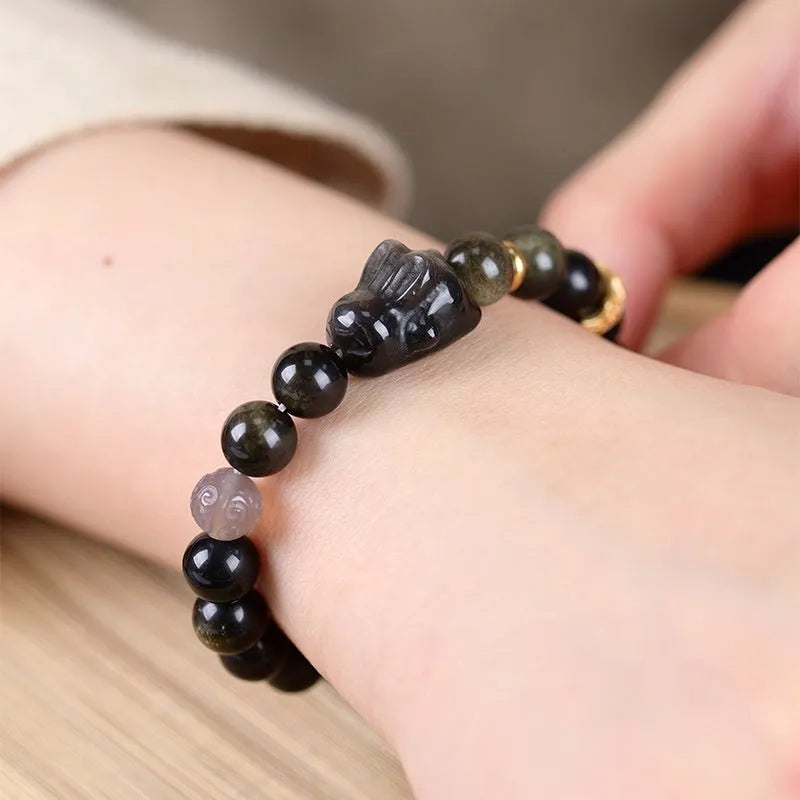 Close-up of a handmade lying rabbit obsidian bracelet in brass with grey agate beads.