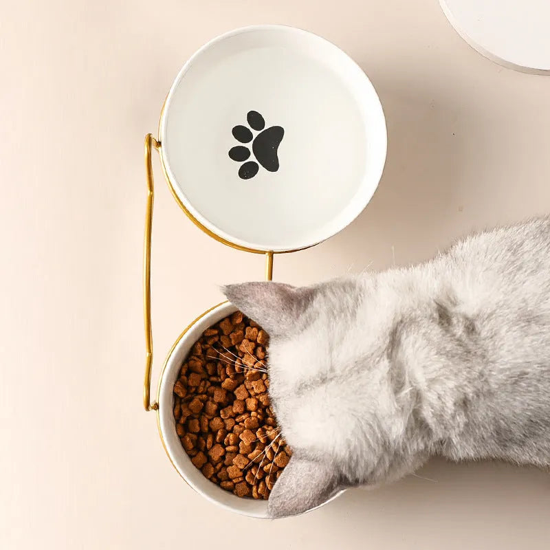 White ceramic cat bowl with cat paw print design sitting in a black iron frame stand