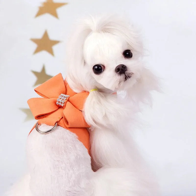 A pink microfiber puppy chest strap harness with a large central bowknot, showing adjustable buckles.