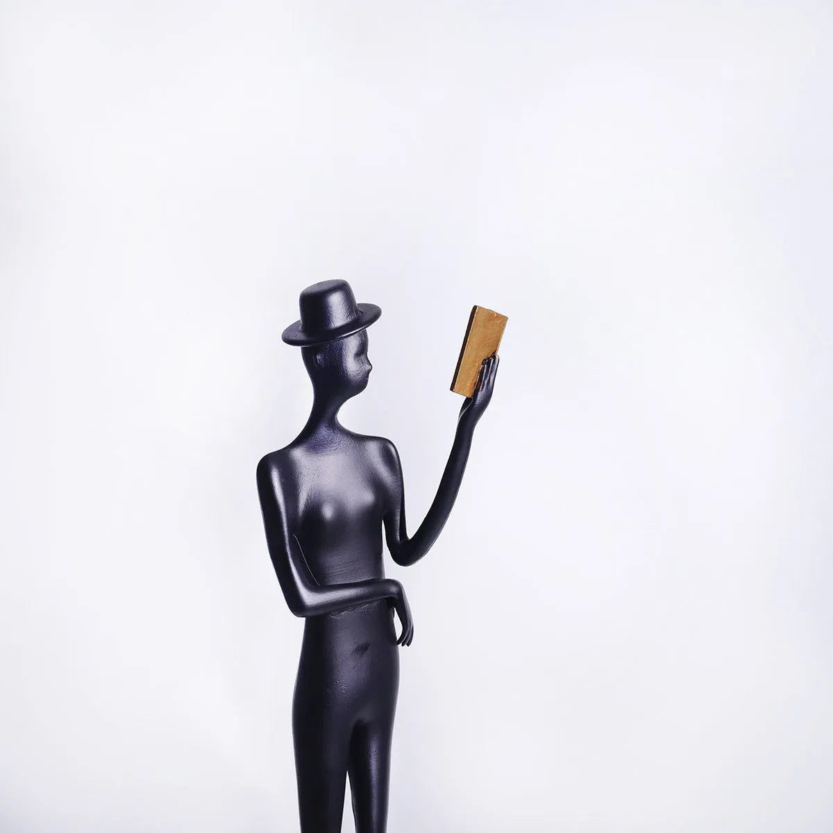Black aluminium desktop sculpture of a woman reading, measuring 12cm wide by 51cm tall.