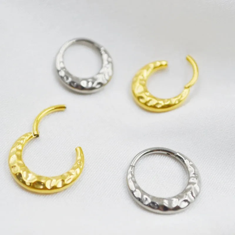 Close-up of a concave-convex titanium nose ring in gold or silver finish, showing textured surface.