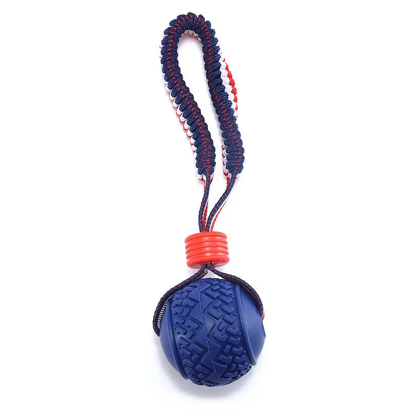 Blue natural rubber dog ball with integrated rope toy on grass, showing textured surface and scale.