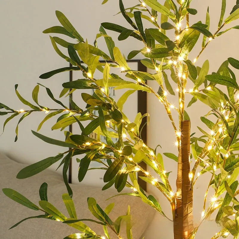 Tall artificial olive tree lamp with warm white LED lights illuminated in an outdoor courtyard setting.