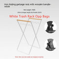 Black folding iron trash rack with wooden handle holding a bin bag outdoors.