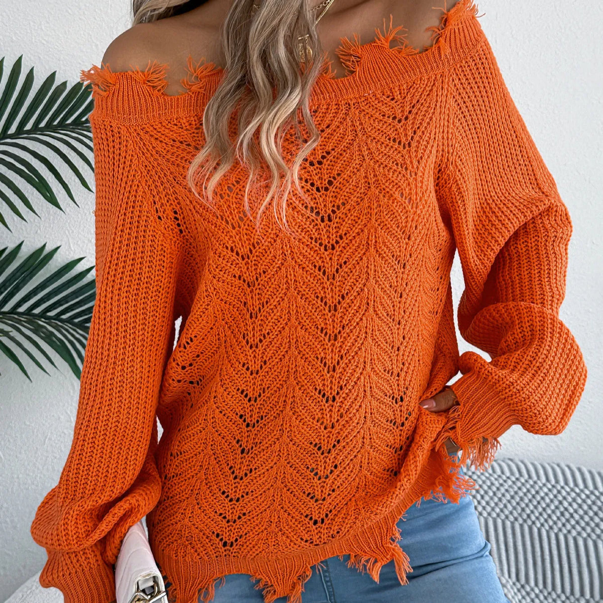 White hollow-out cut off-the-shoulder long sleeve pullover sweater on a hanger showing acrylic knit fabric detail.