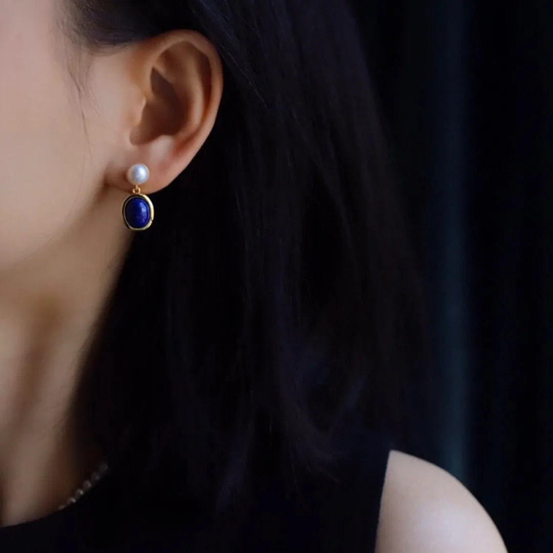 A pair of 925 sterling silver stud earrings with a deep blue lapis lazuli pearl and auspicious pattern details.