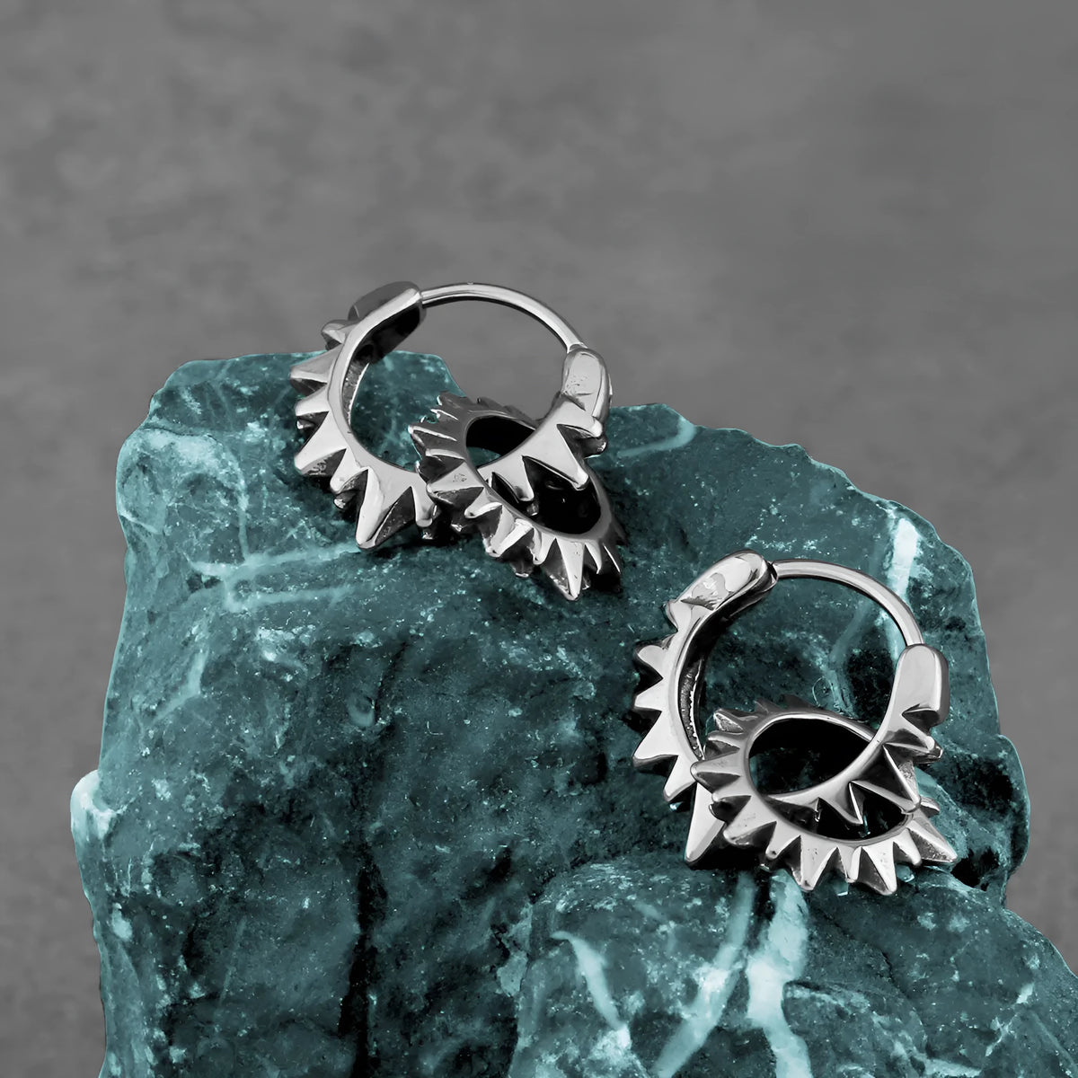 A pair of simple, polished stainless steel round ring hoop earrings on a steel colour background.