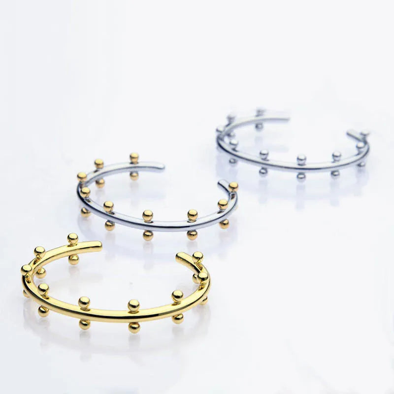 C-shaped stainless steel alloy bracelet with textured rivet-shaped beads on a wrist.