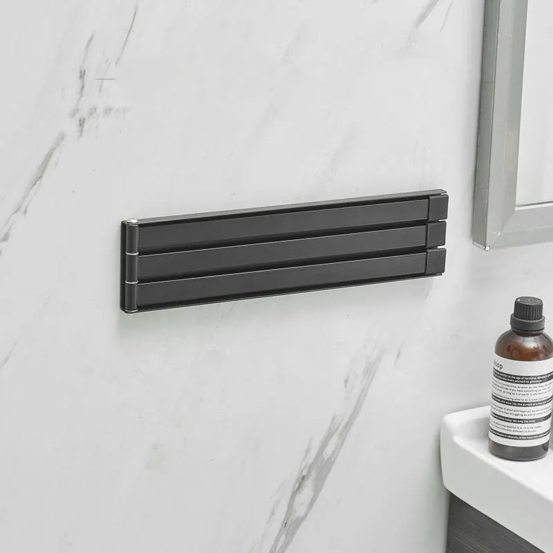 Black folding towel rack mounted on bathroom wall with towel hanging