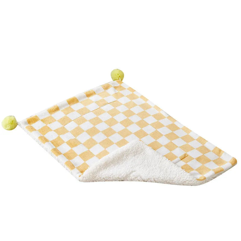 Green plaid pet blanket with fur ball trim on a sofa with a cat resting on it.