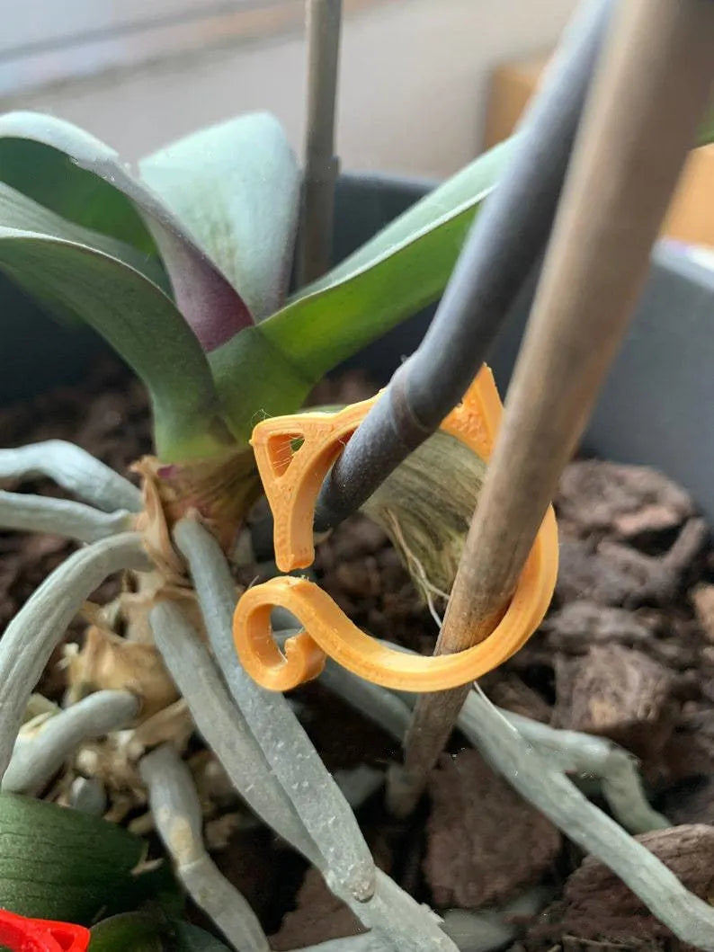 Colourful plastic cat-shaped plant clip for gardening support on a green leaf.