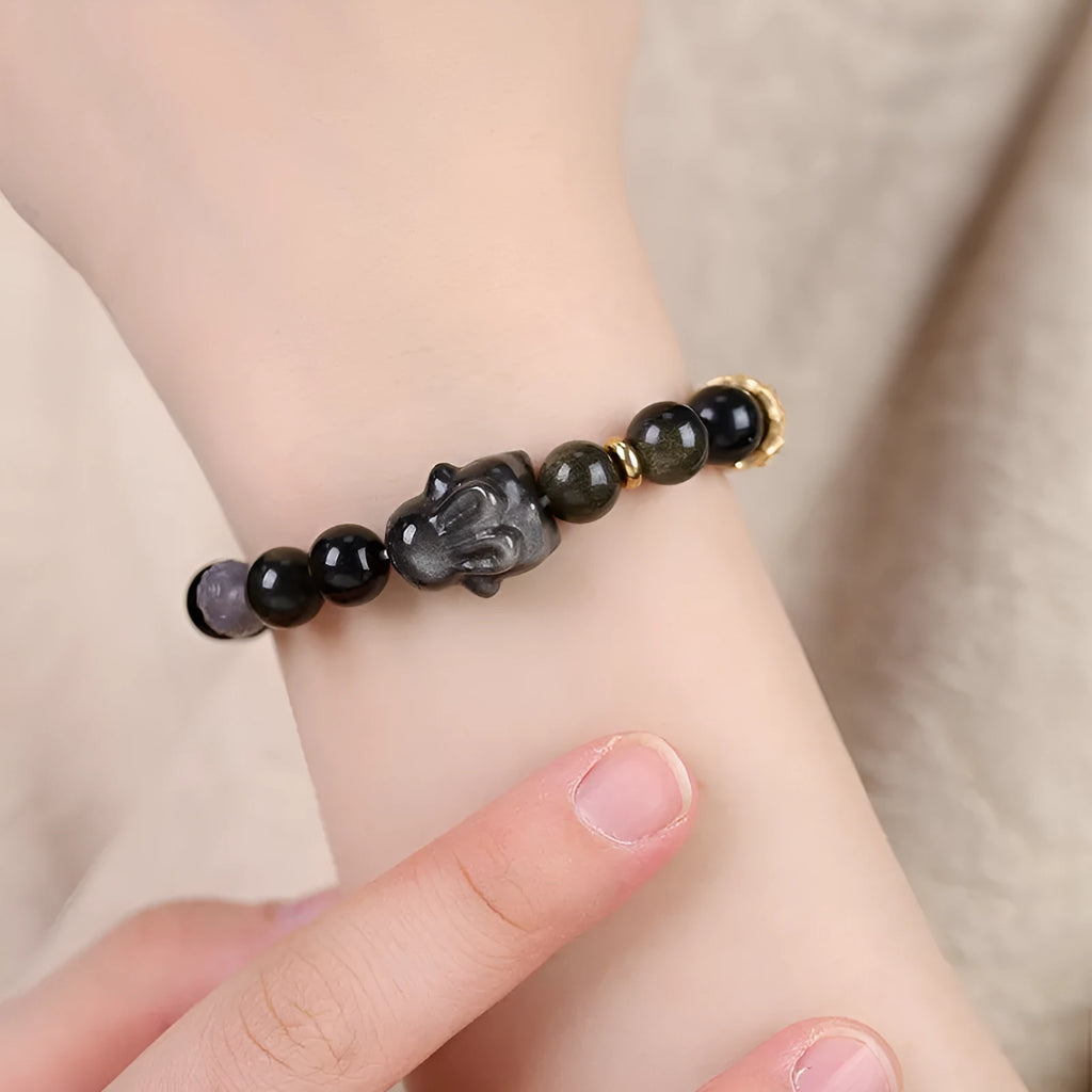 Close-up of a handmade lying rabbit obsidian bracelet in brass with grey agate beads.