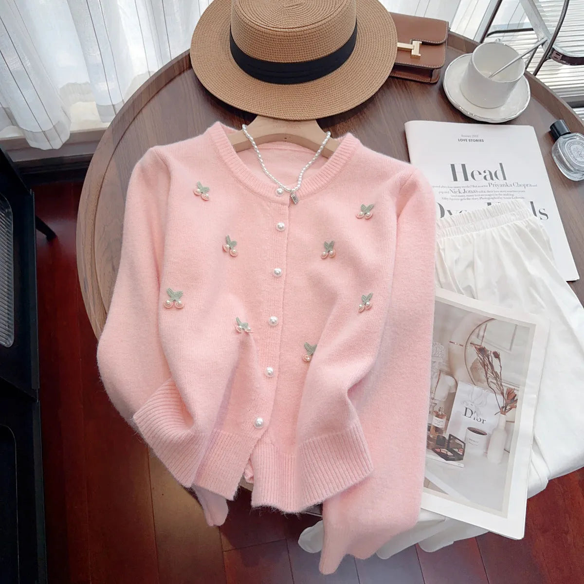 A pink cashmere blend ladies cardigan with beaded details, shown on a hanger.