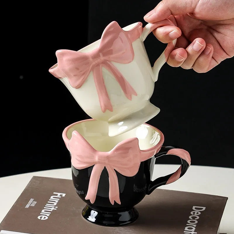 Cute white ceramic mug with a black heart bow design and printed handle ornament.