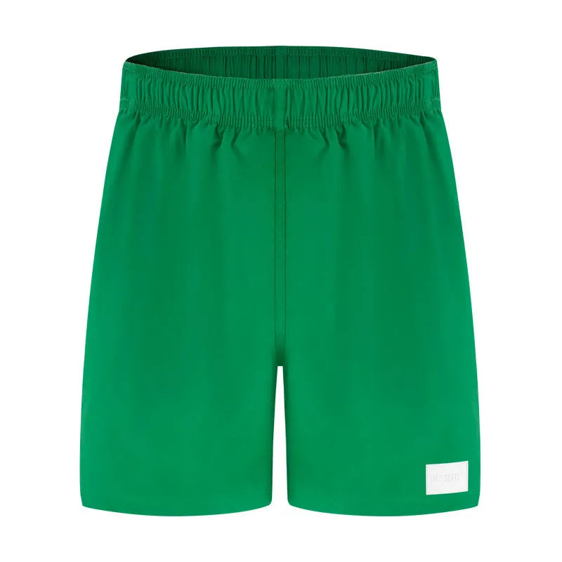 Man wearing solid green quick-drying nylon shorts with a straight leg opening on a beach.