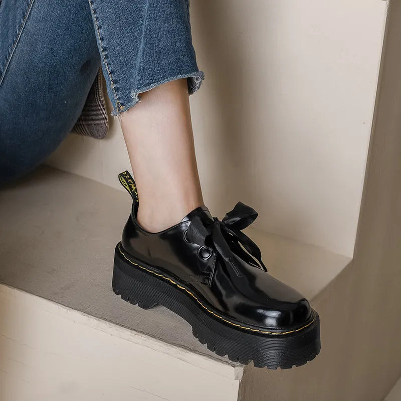 Black women's thick-soled leather lace-up shoes with a cross strap design on a white background.