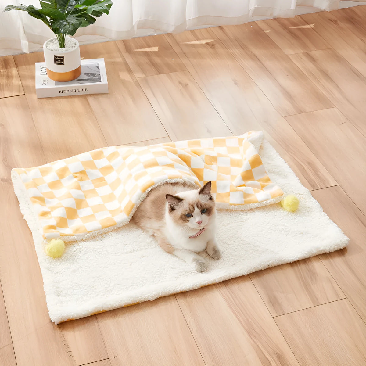 Green plaid pet blanket with fur ball trim on a sofa with a cat resting on it.