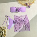 Women's pink tube top swimsuit with large three-dimensional flower tie, matching skirt and pants laid flat.