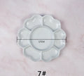 White ceramic plum blossom shaped artist's paint palette on a wooden table.