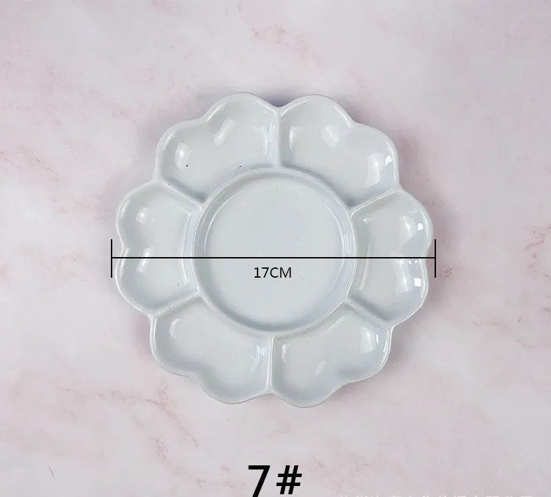 White ceramic plum blossom shaped artist's paint palette on a wooden table.