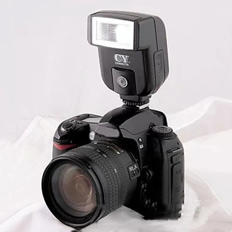 Compact silver hot shoe camera flash with head tilted upwards, shown next to two AA batteries for scale.