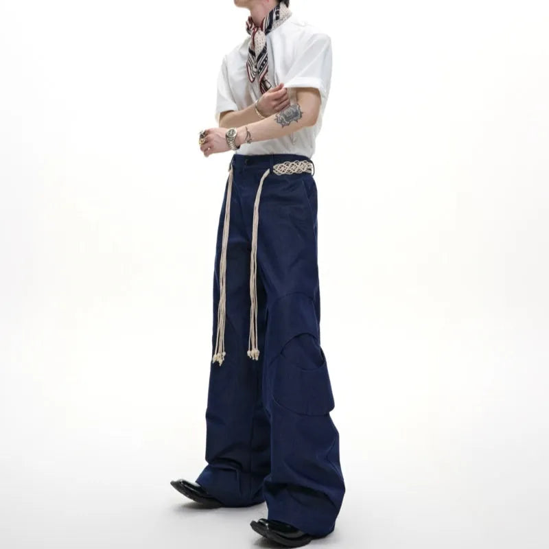 Men's dark blue loose straight-leg jeans with 3D cutting, heavy belt stitching, and pocket tassel details.