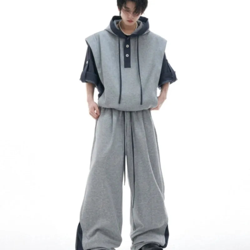 Man wearing a grey hooded short-sleeve sports jacket with textured stitching and black trousers.