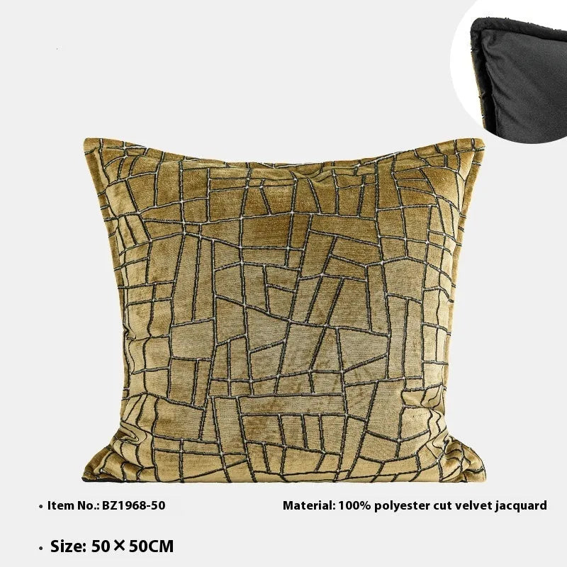 Gold geometric abstract pattern on a velvet square decorative cushion on a grey sofa.