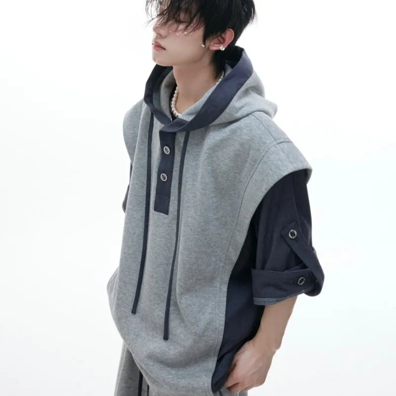 Man wearing a grey hooded short-sleeve sports jacket with textured stitching and black trousers.
