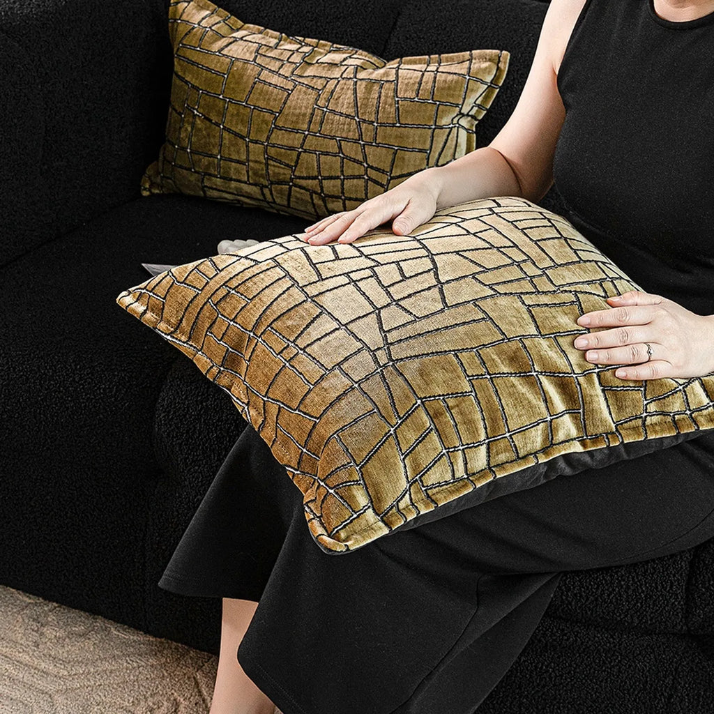 Gold geometric abstract pattern on a velvet square decorative cushion on a grey sofa.