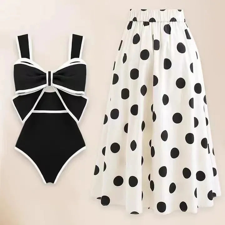 Women's black one-piece swimsuit with white round skirt and bow, worn as a beach dress.