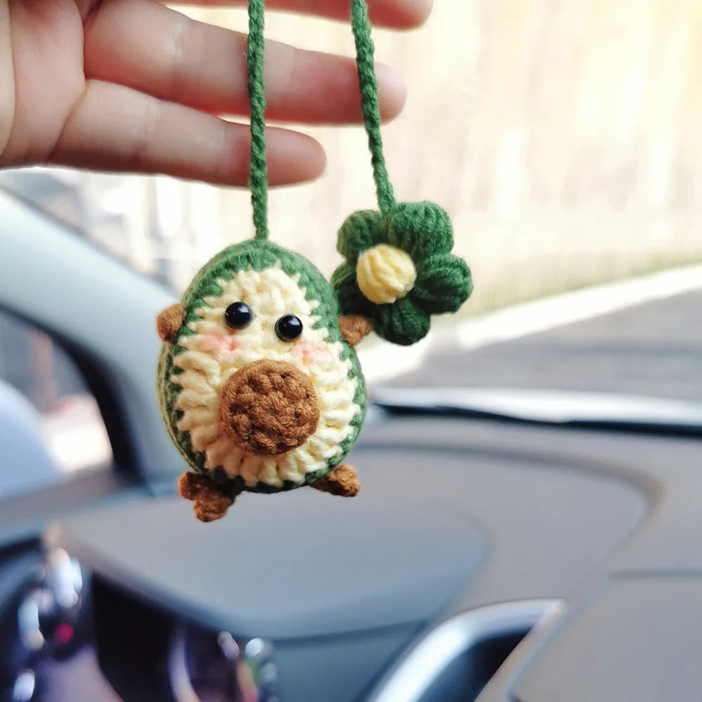 Handmade crocheted avocado-shaped car pendant with rainbow pattern, hanging.