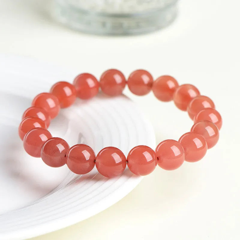 Loose polished cherry red agate beads in various sizes for bracelet making on a white surface.